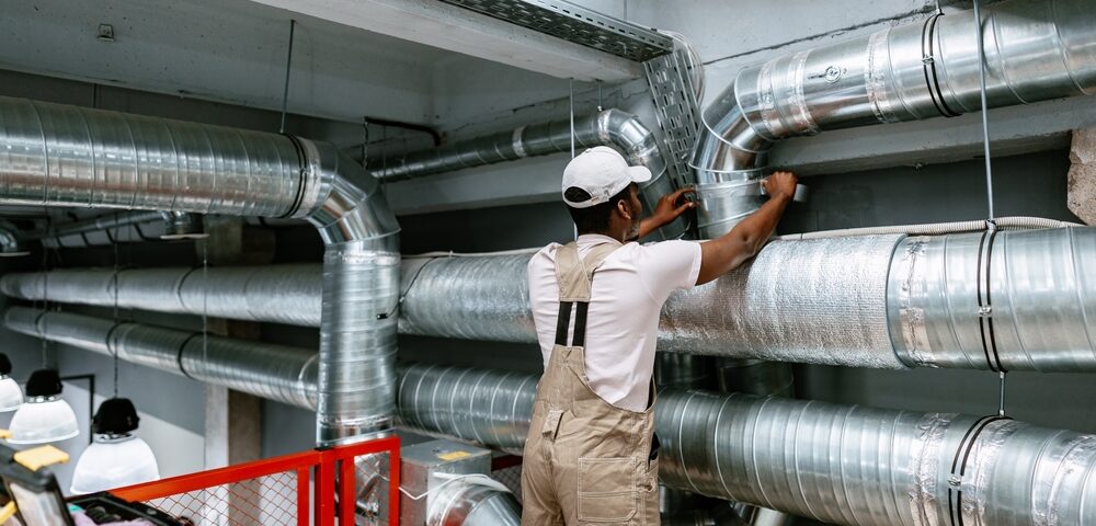 Worker,Installing,Ventilation,Ductwork,In,Industrial,Setting,During,Daytime,At